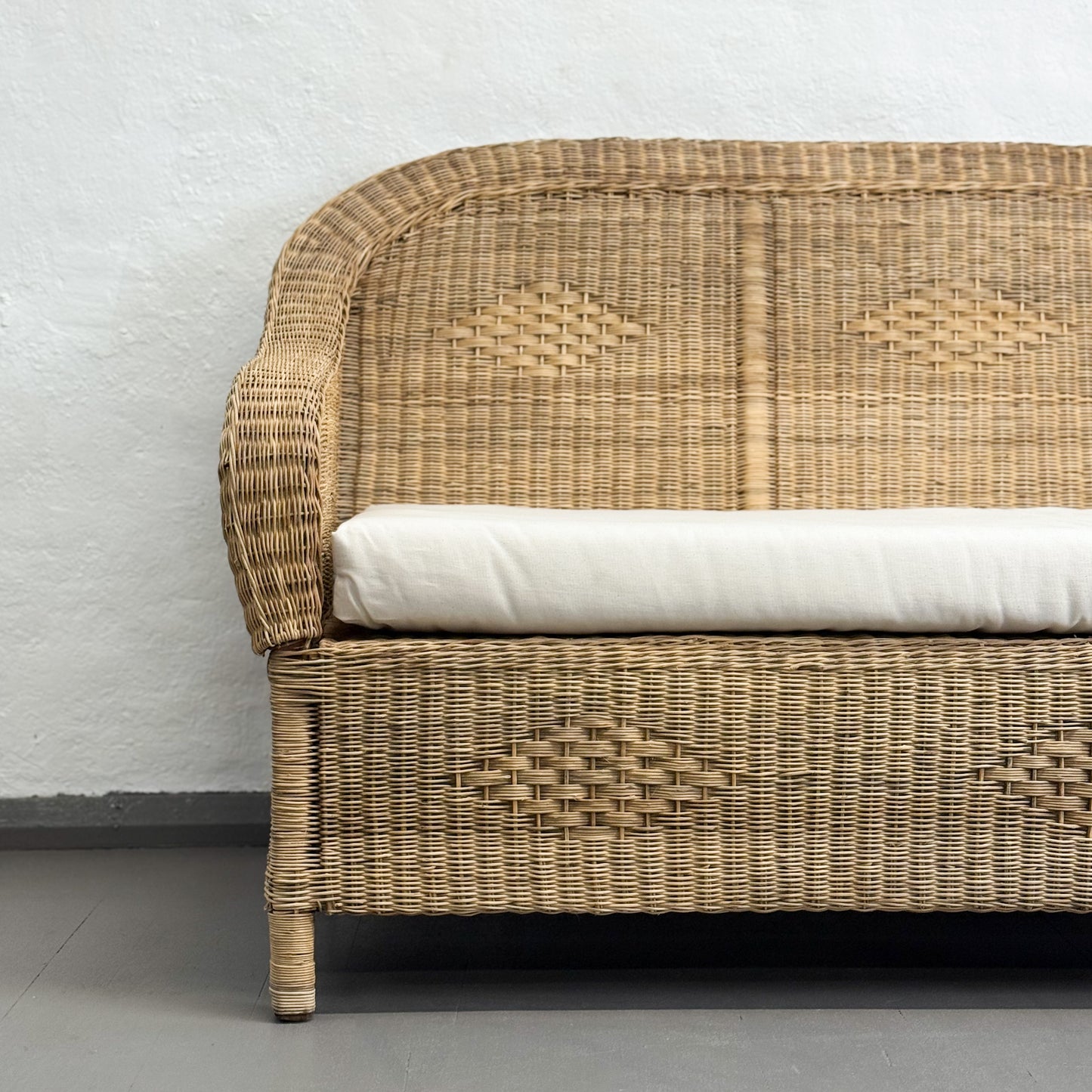 Wicker sofa with a white cushion against a plain wall.
