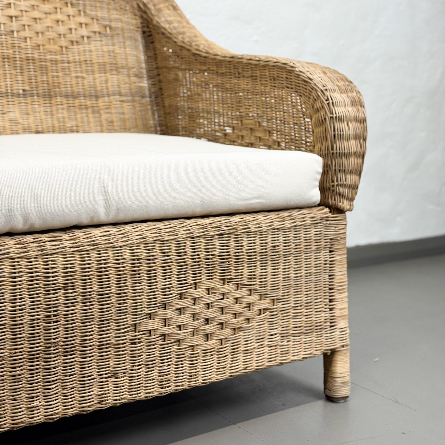 Wicker chair with a white cushion on a gray floor and white wall background