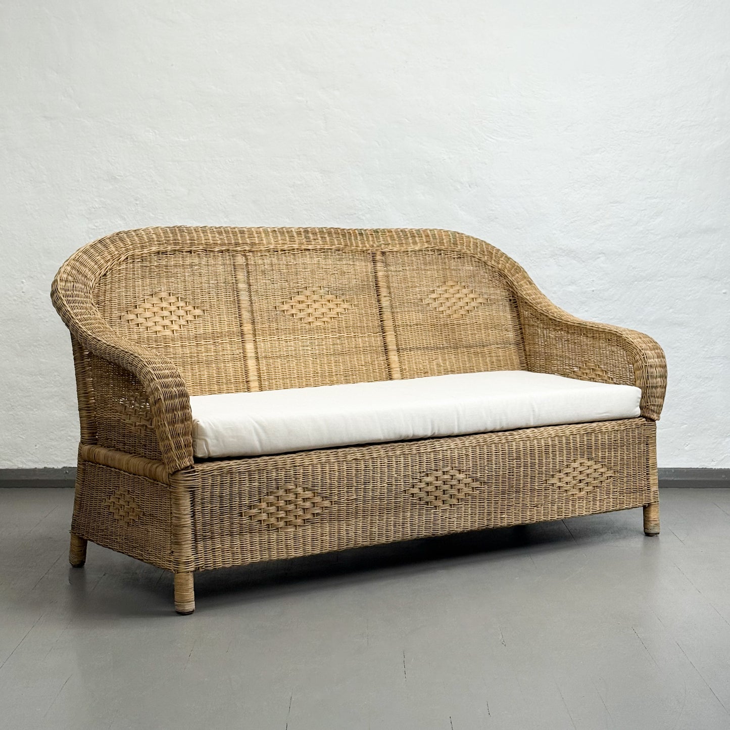 Wicker sofa with white cushion on a gray floor and light gray wall