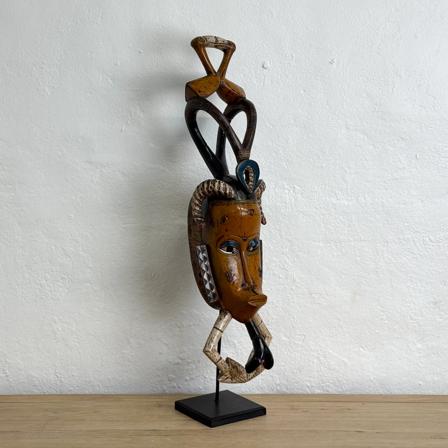 Wooden mask on a stand against a white wall