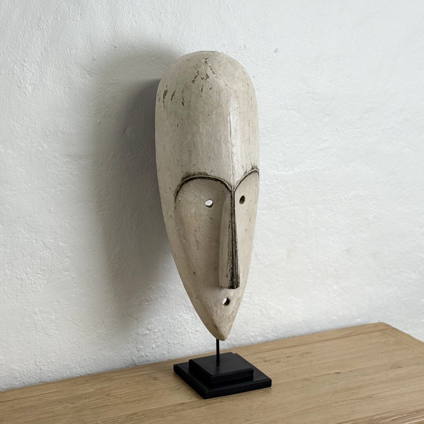 Abstract stone mask on a stand against a white wall