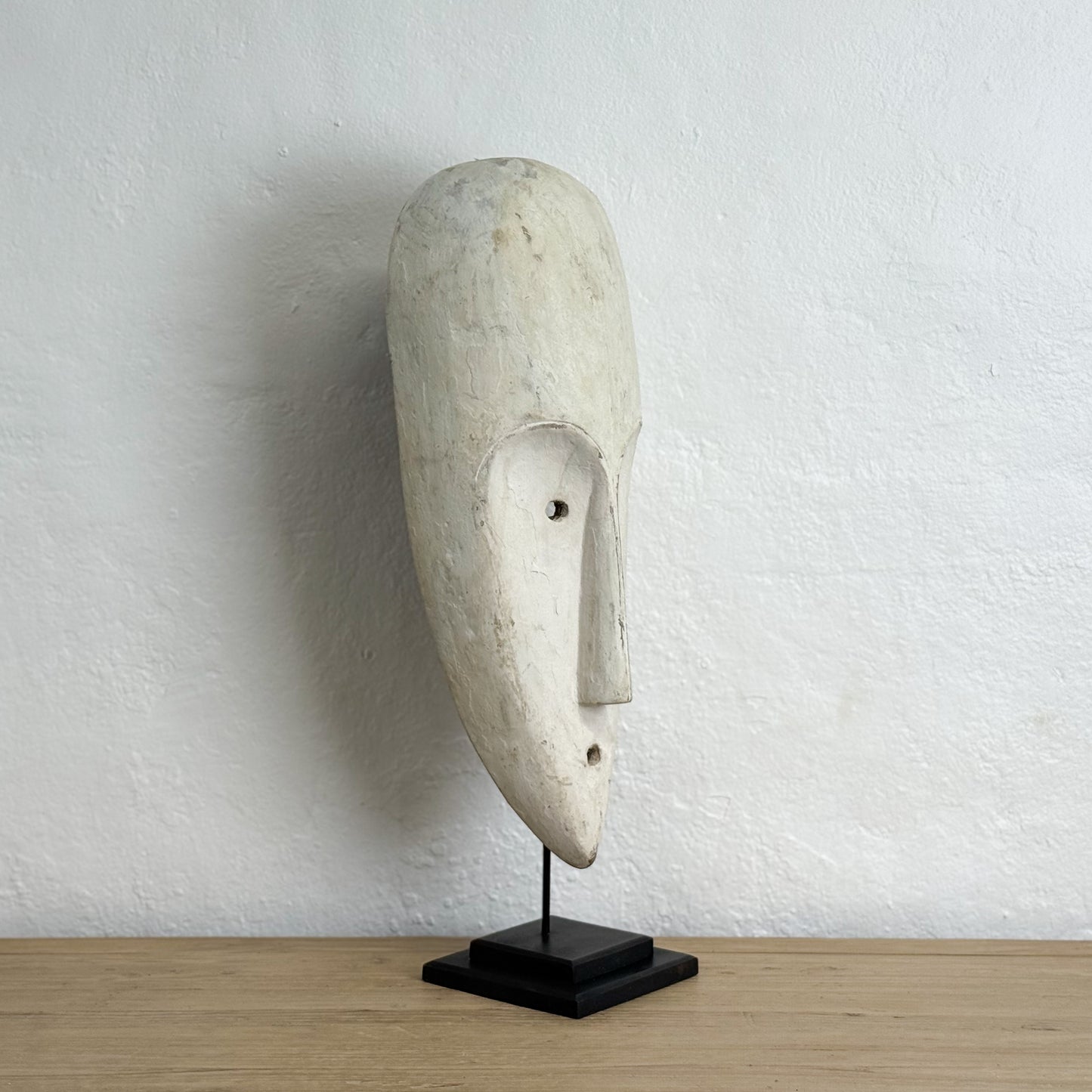 Stone mask on a stand against a textured white wall