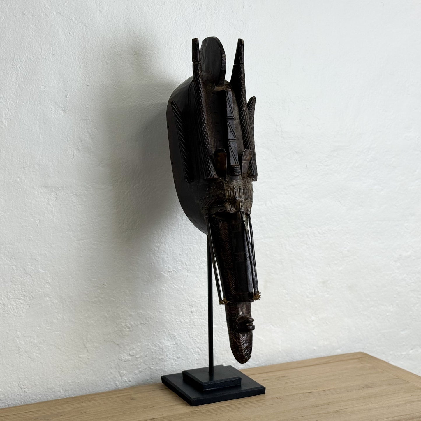 Wooden mask on a stand against a white wall