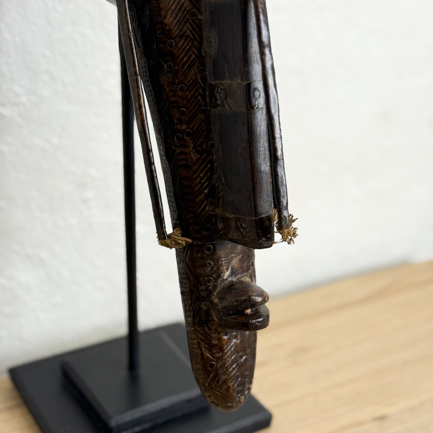 Carved wooden mask on a stand against a white wall