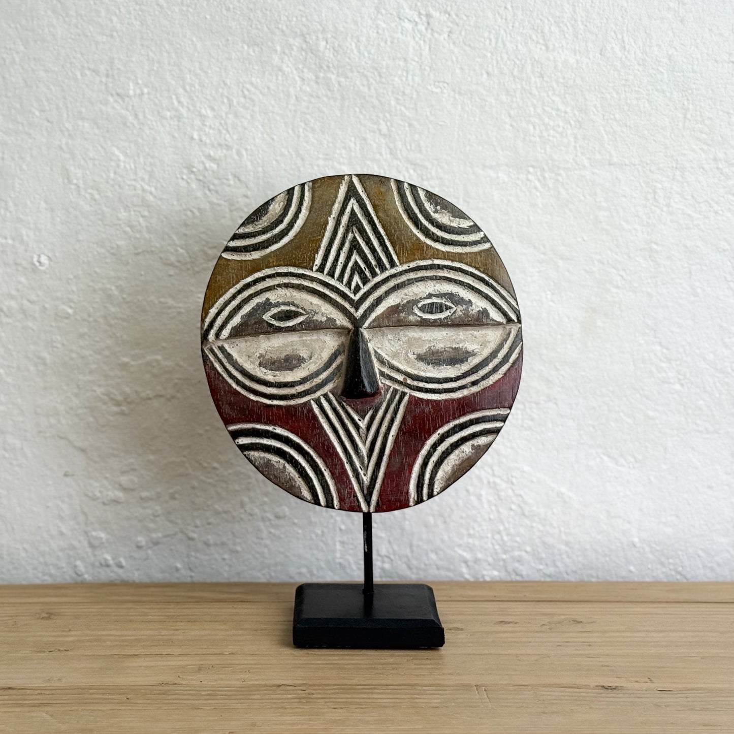 Decorative mask on a stand against a white wall