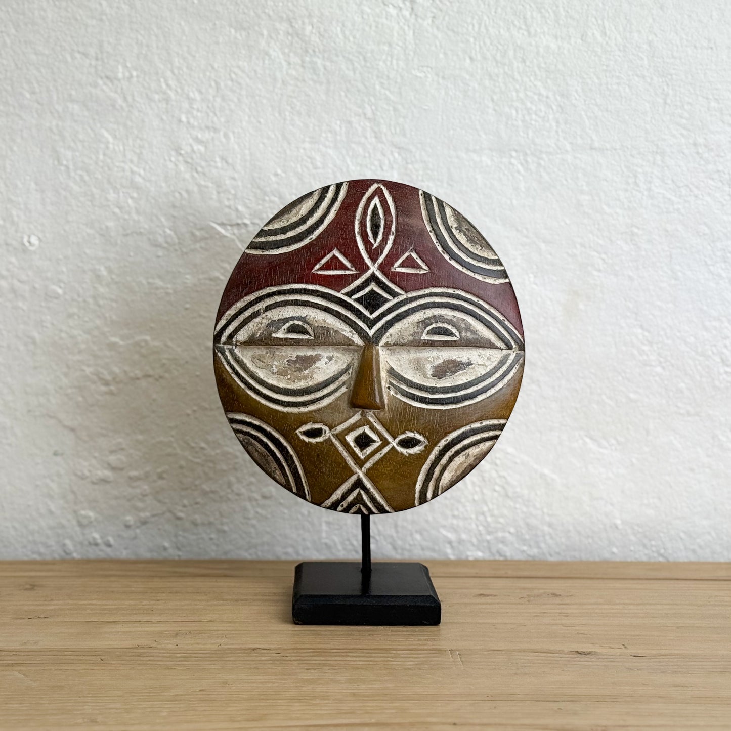 African-style mask on a stand against a white wall.