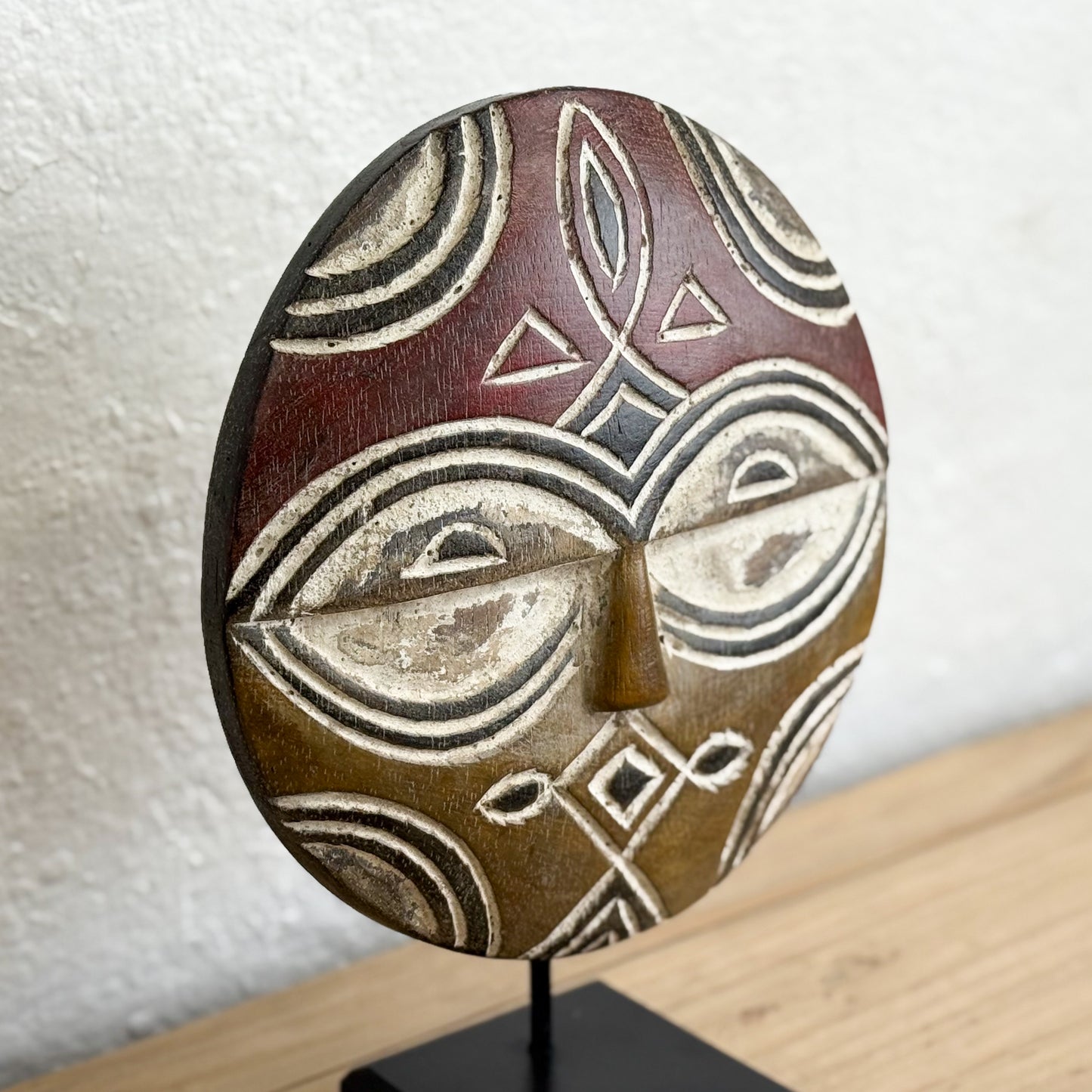 Ceramic mask with geometric patterns on a stand against a neutral background