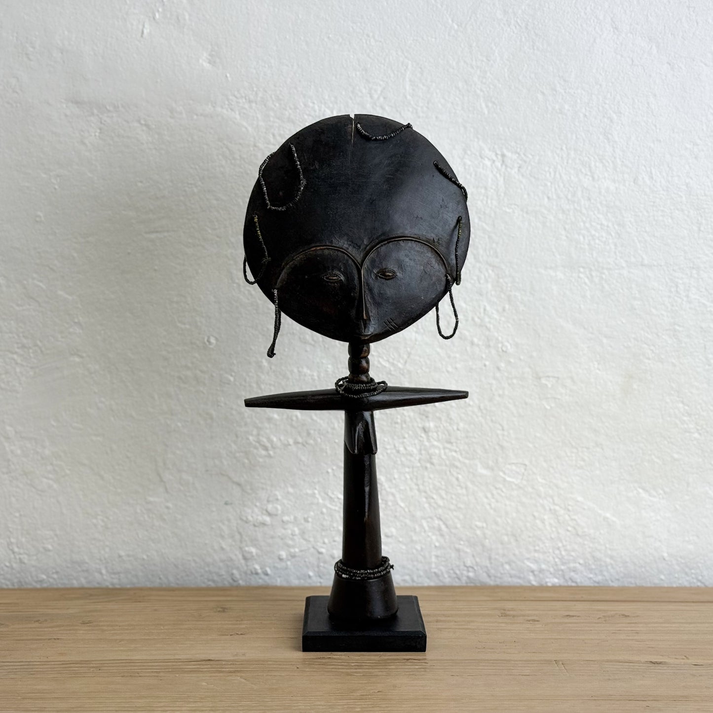 Black metal sculpture on a wooden surface with a white textured wall background