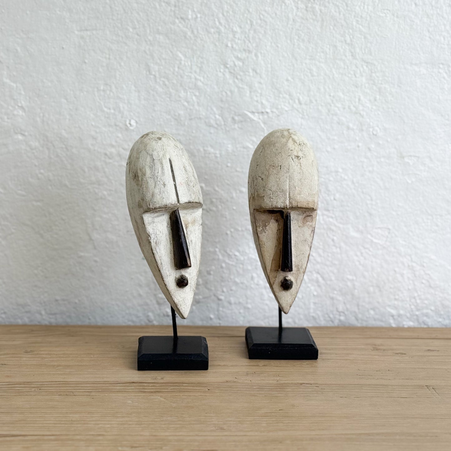 Two stone face masks on stands against a white wall.