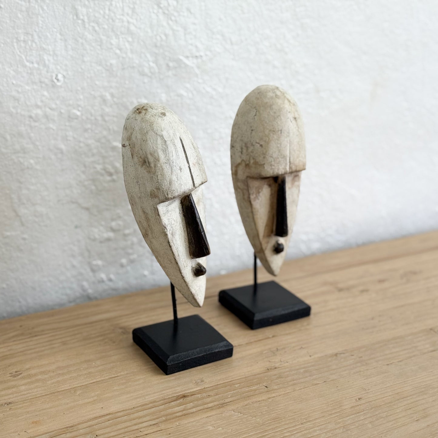 Two wooden masks on stands against a white wall