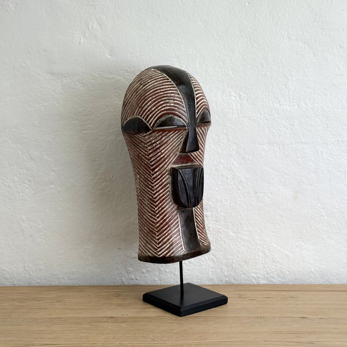 Wooden mask on a stand against a white wall