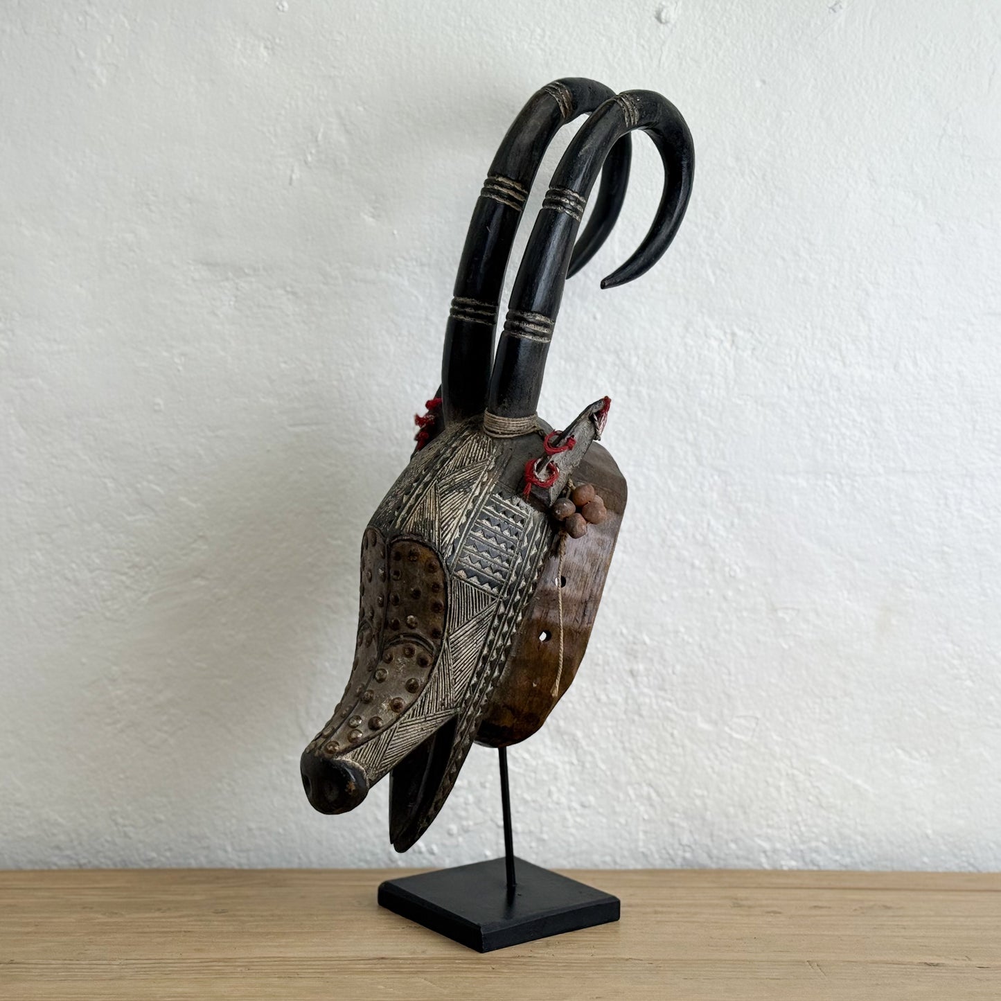 Decorative animal head with large horns on a stand against a white wall.