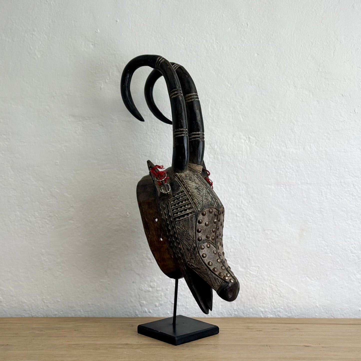 Decorative mask with curved horns on a stand against a white wall.