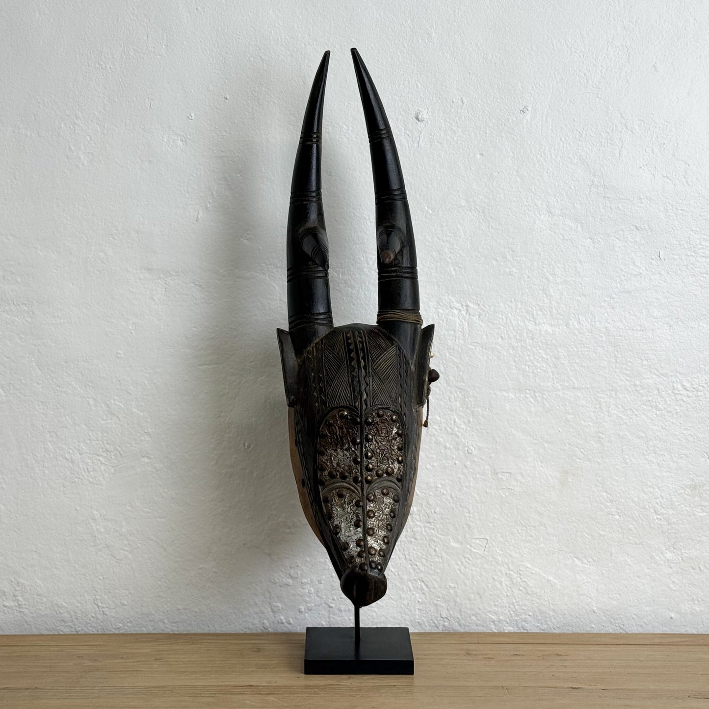 Decorative mask with large horns on a stand against a white wall