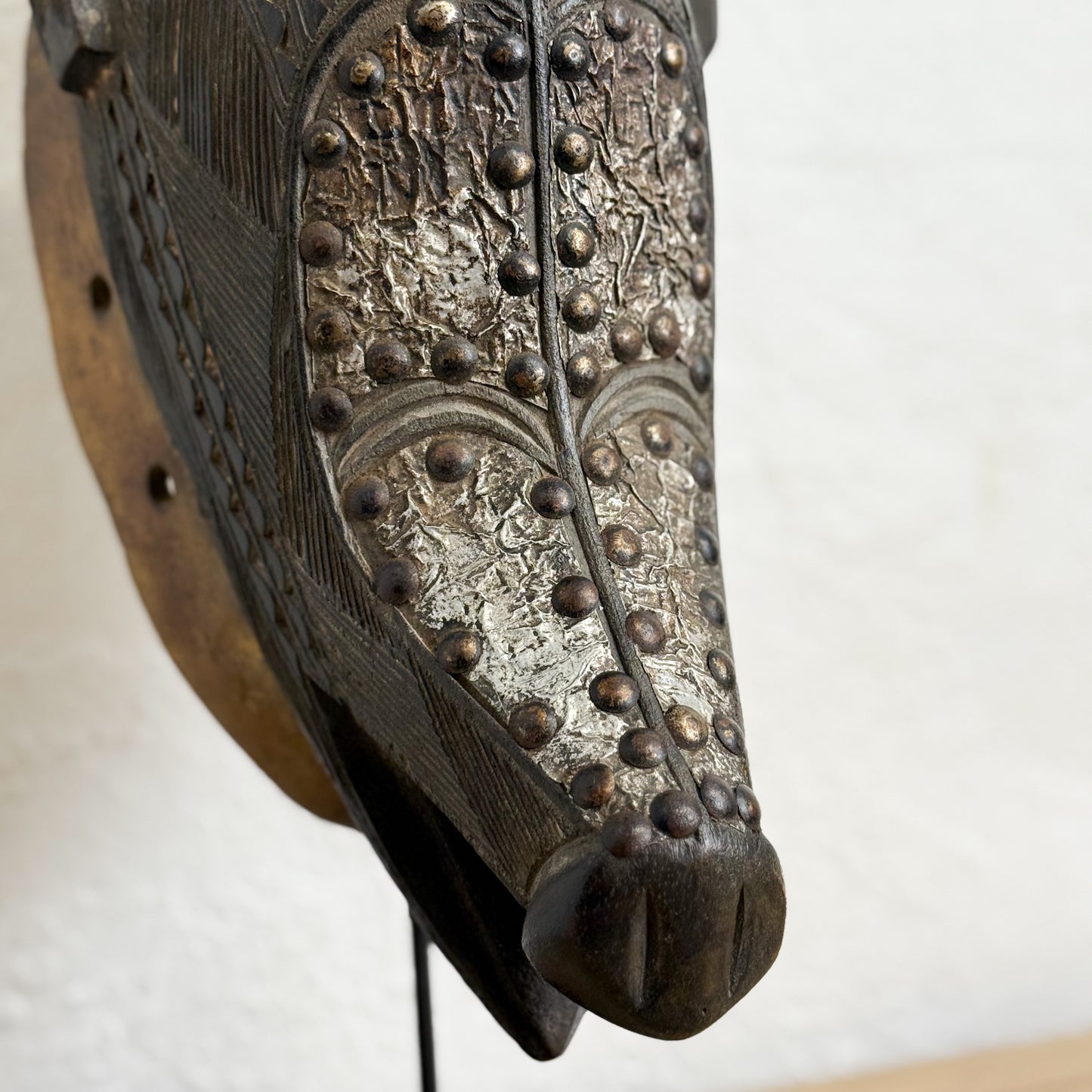Decorative horse head mask with intricate details and studded embellishments on a plain background