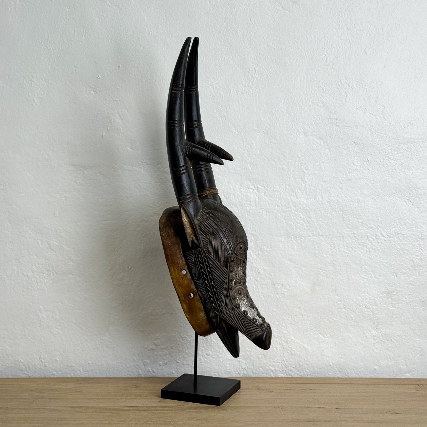 Wooden mask on a stand against a white wall