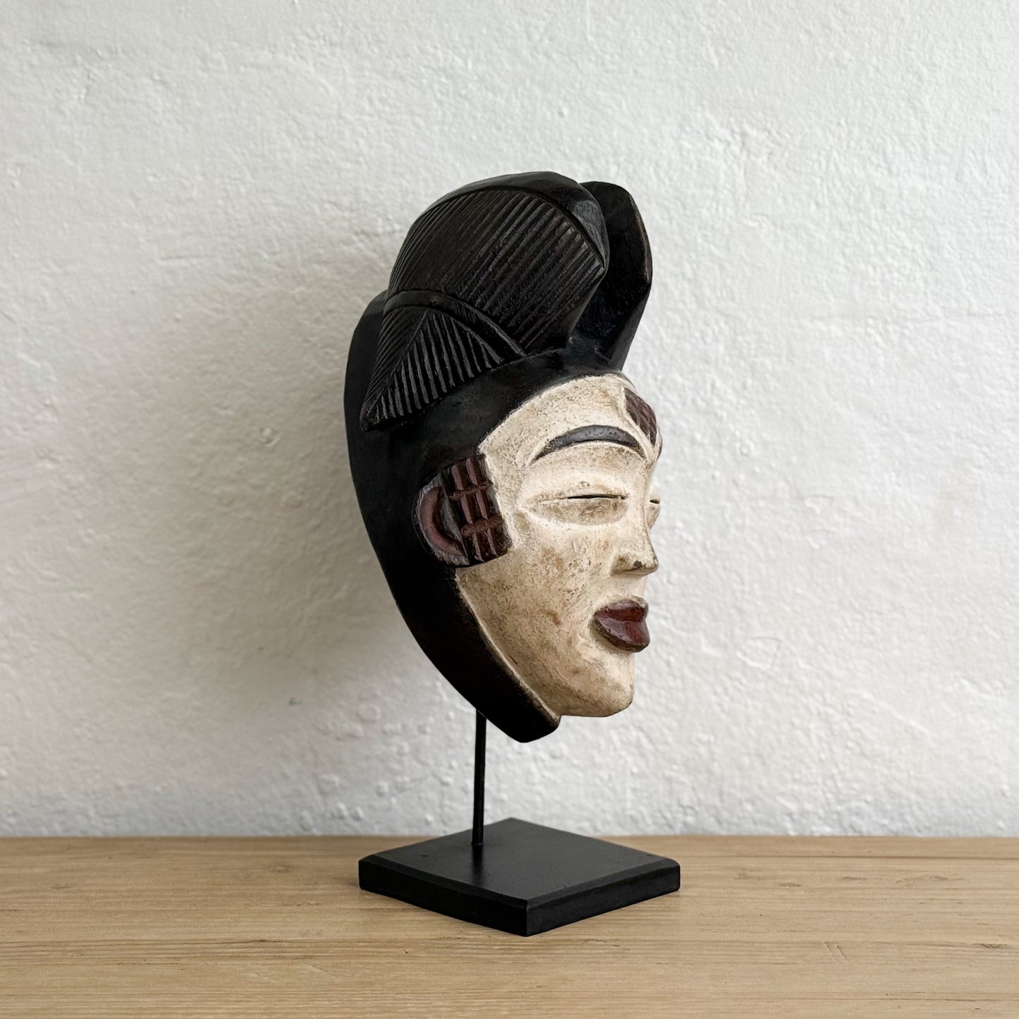 Decorative mask on a stand against a white textured wall