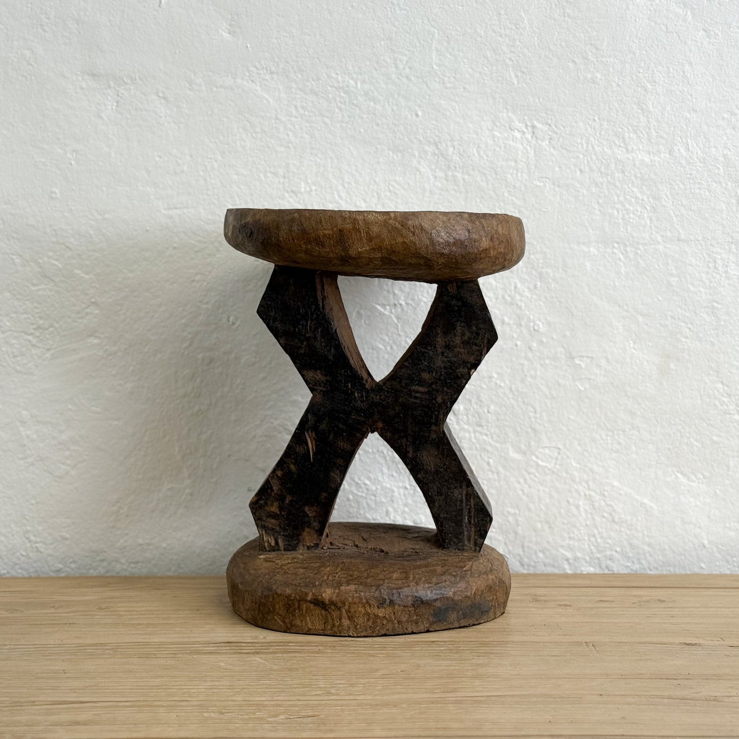 Wooden stool with a unique design on a wooden surface and white wall background