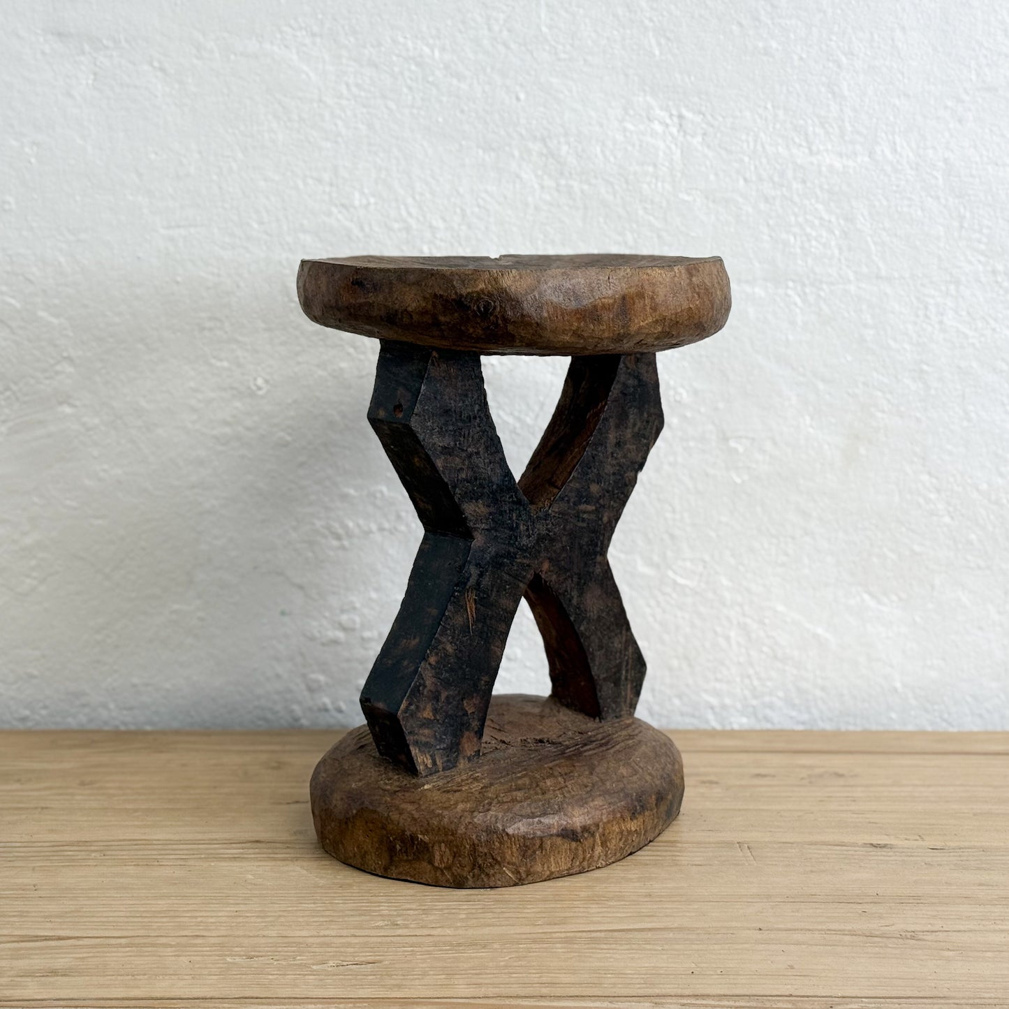 Wooden stool with a unique design on a wooden surface and white wall background