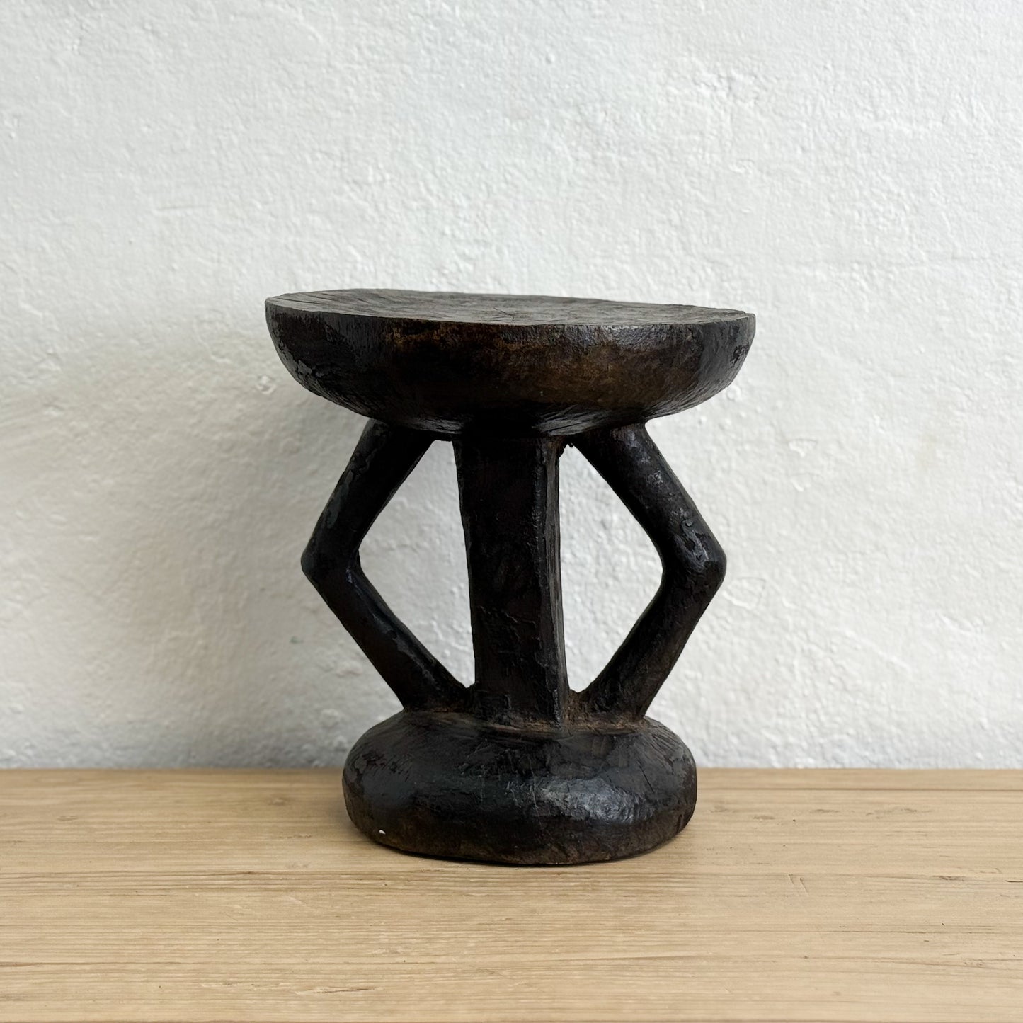 Black wooden stool on a light wood surface with a white textured wall background