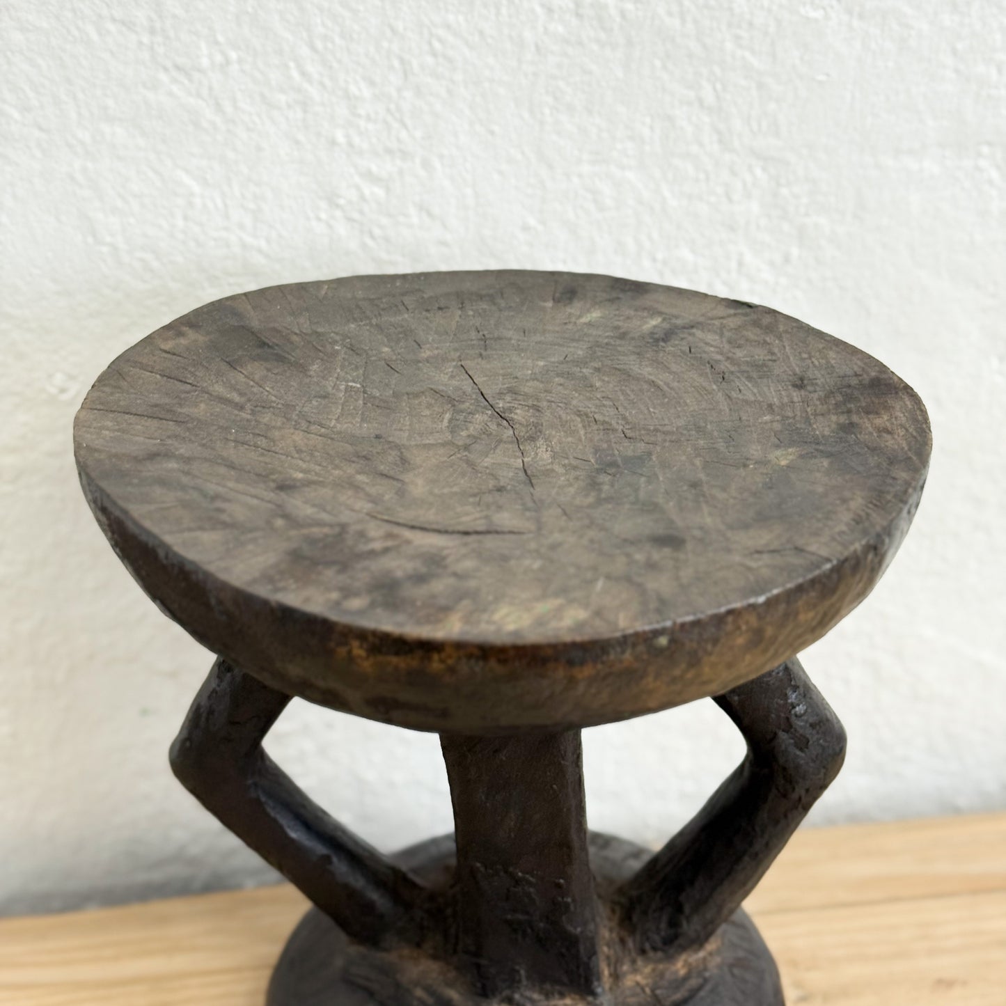 Wooden stool with a round top and unique base design on a light wooden surface.