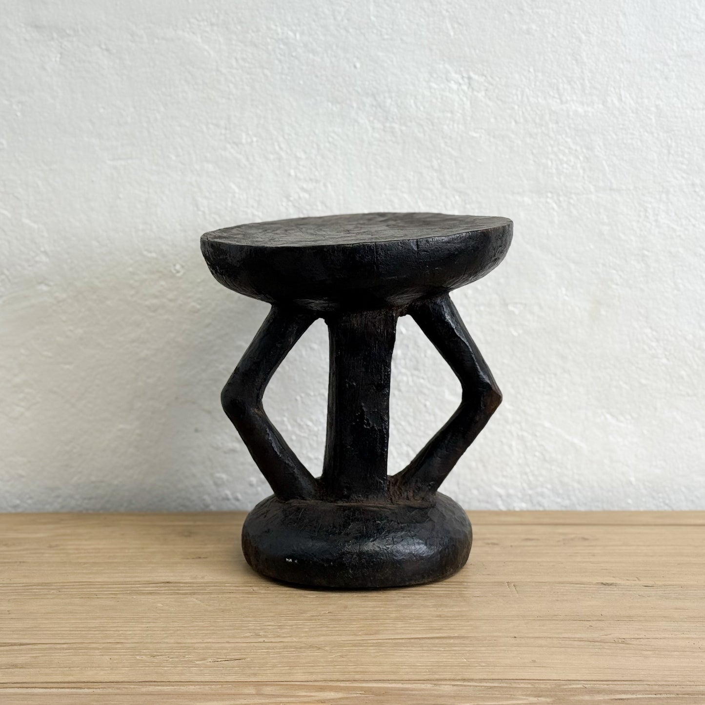 Black stone stool on a wooden surface with a white textured wall background