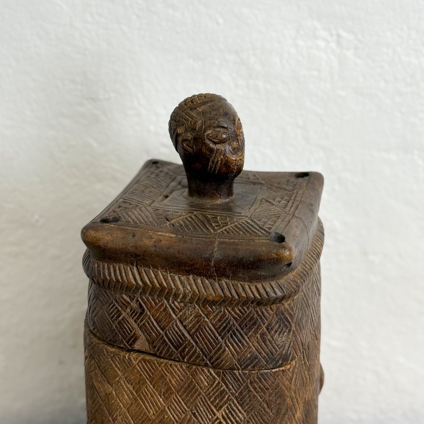 Wooden container with a lid featuring a carved face on a white background