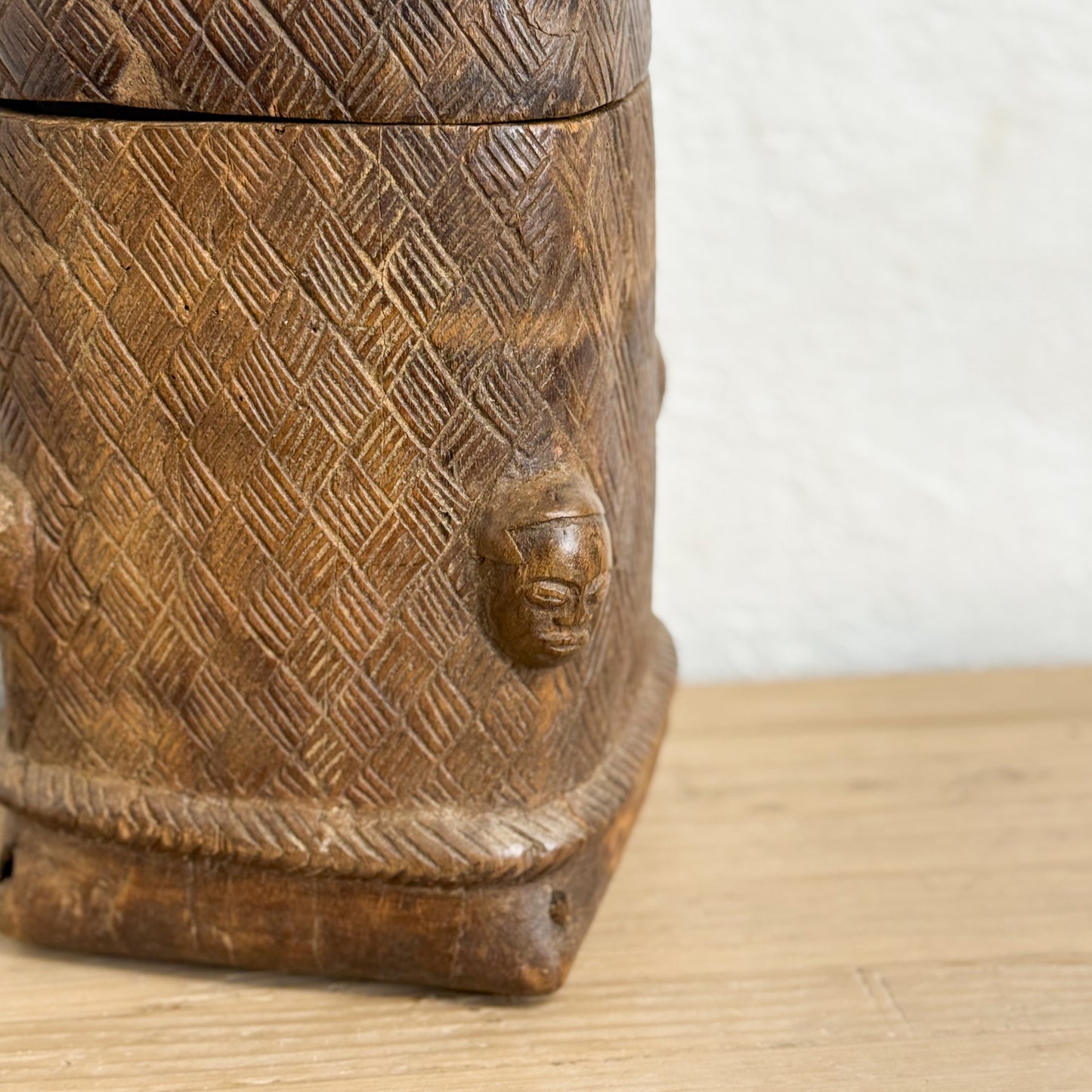 Wooden container with geometric patterns and a face carving on a wooden surface.