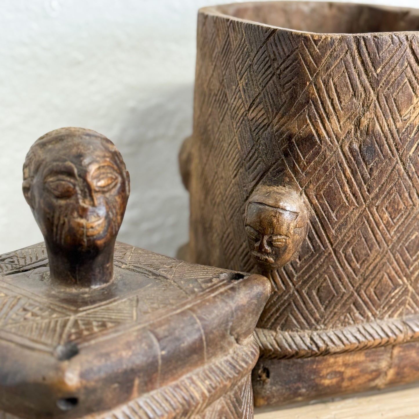 Two intricately carved wooden containers with face-like designs on a neutral background