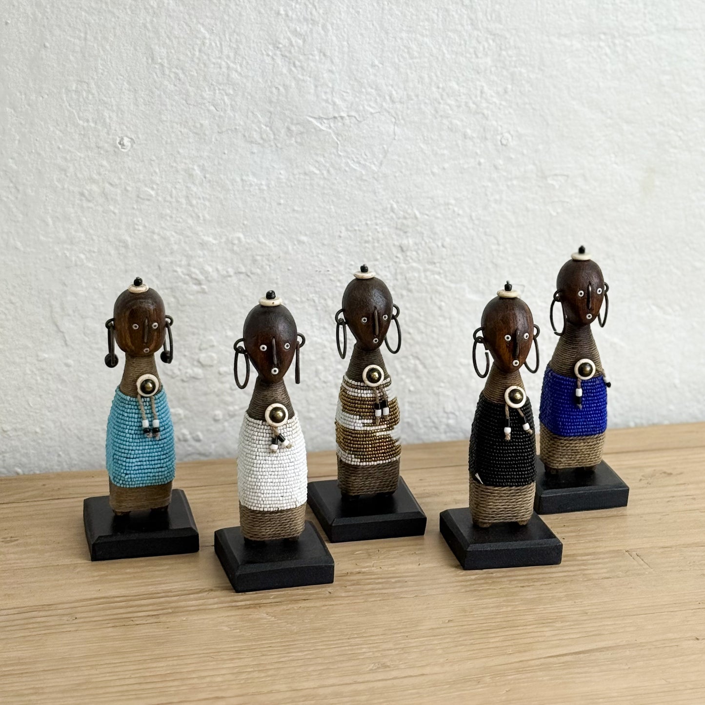 Five decorative figurines of women on stands against a white wall.