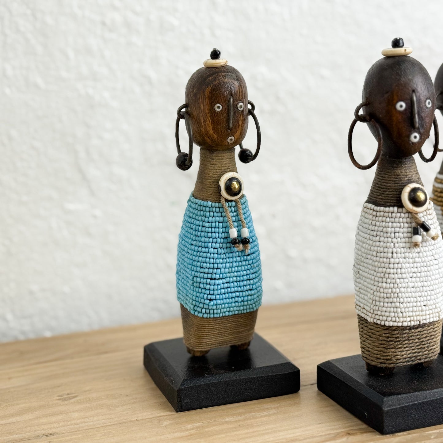 Two decorative figurines with beaded dresses on a wooden surface.