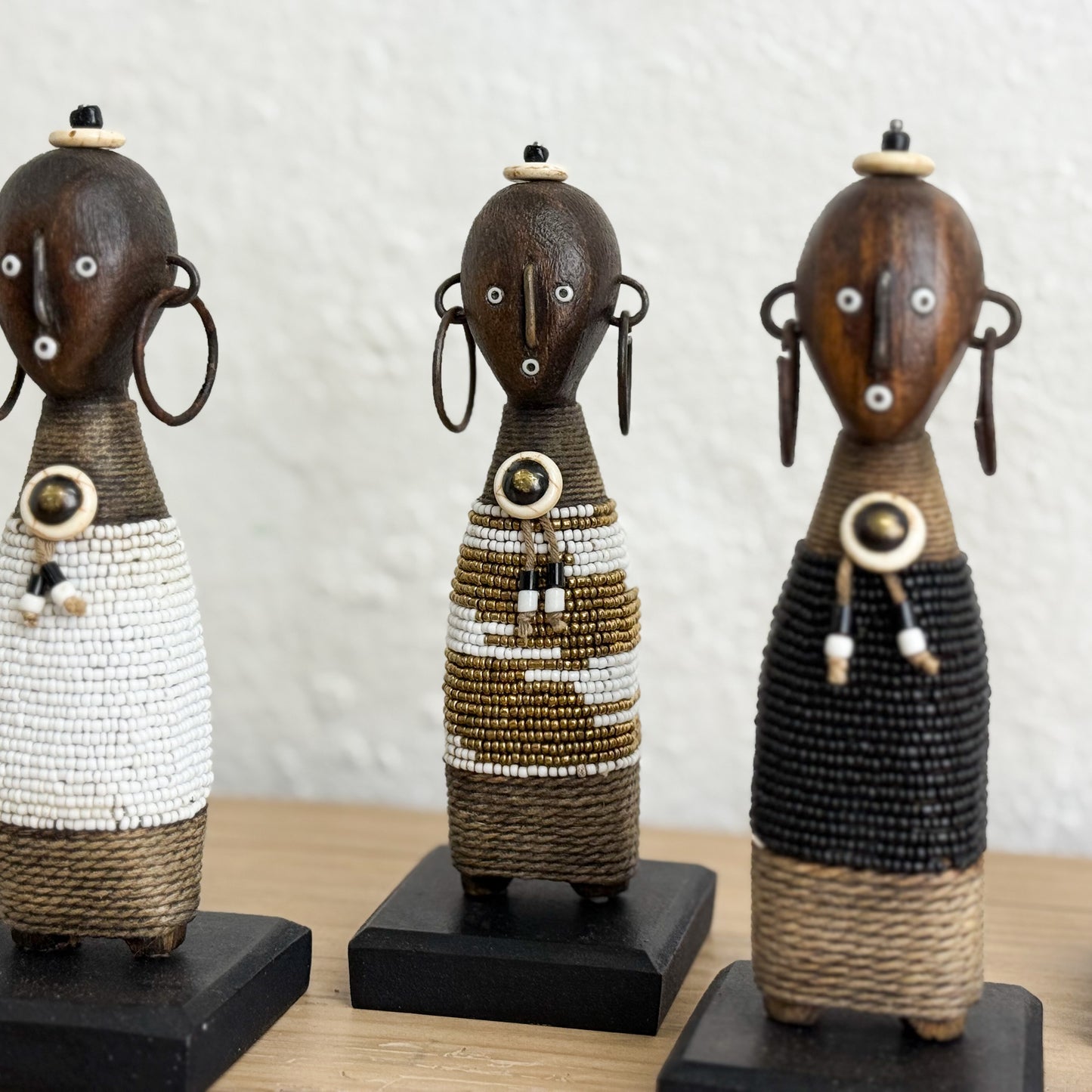 Three decorative figures with beaded dresses on a wooden surface.