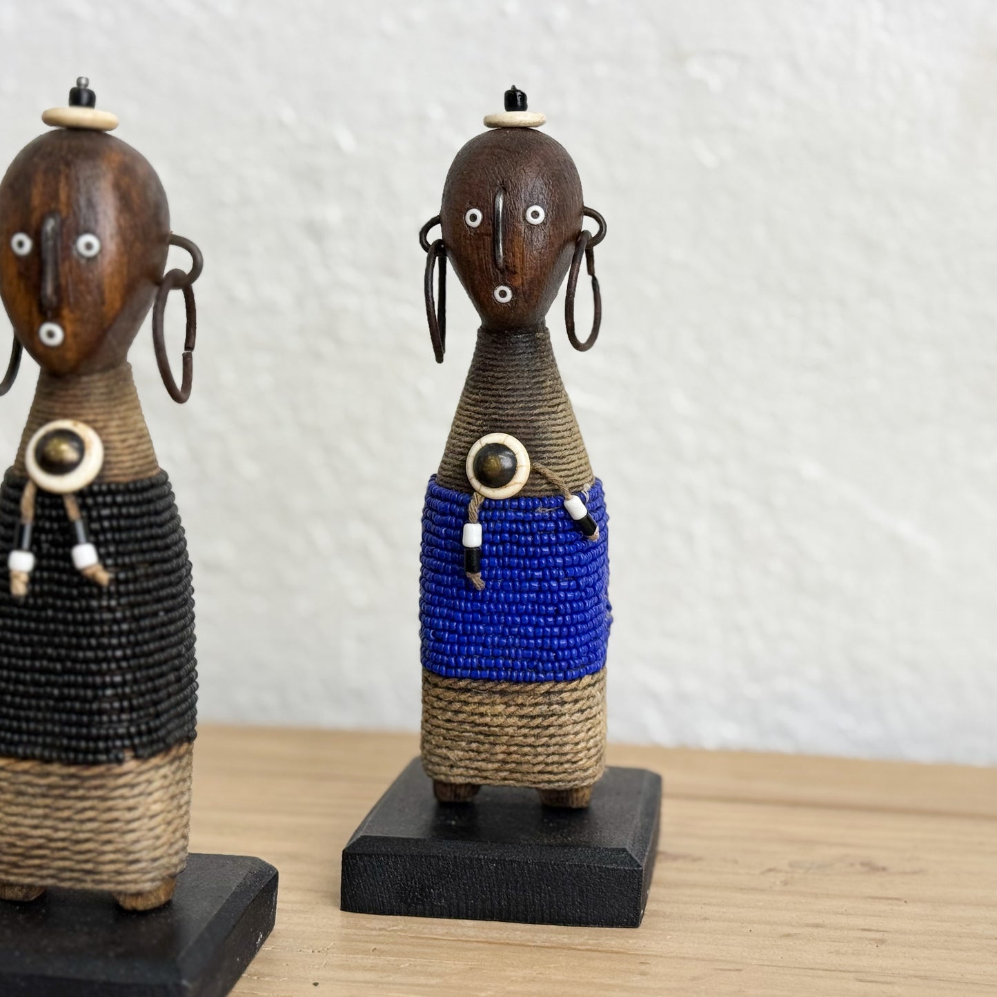 Two wooden figurines with beaded details on a wooden surface and white background