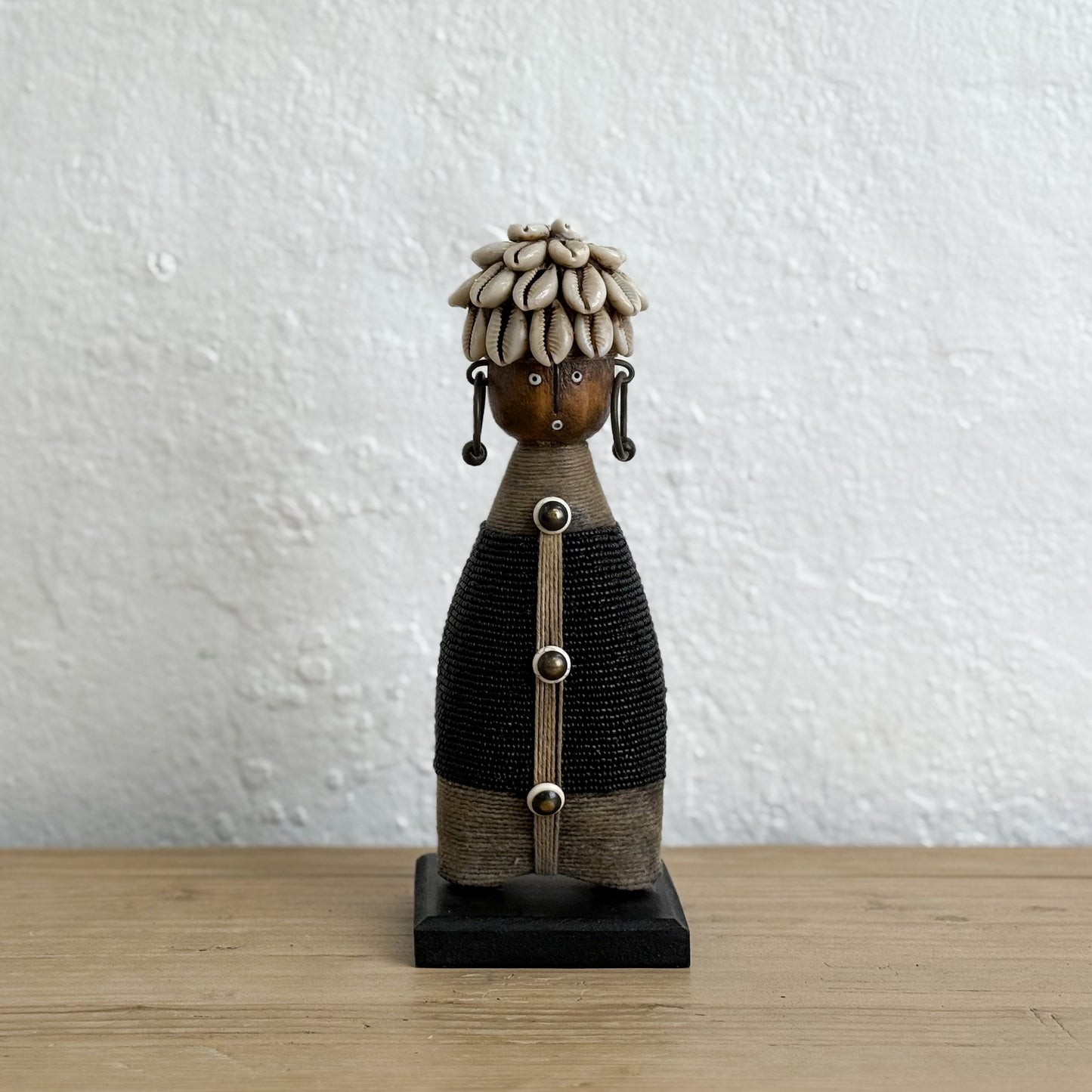 Decorative figure with braided hair on a wooden surface and white wall background