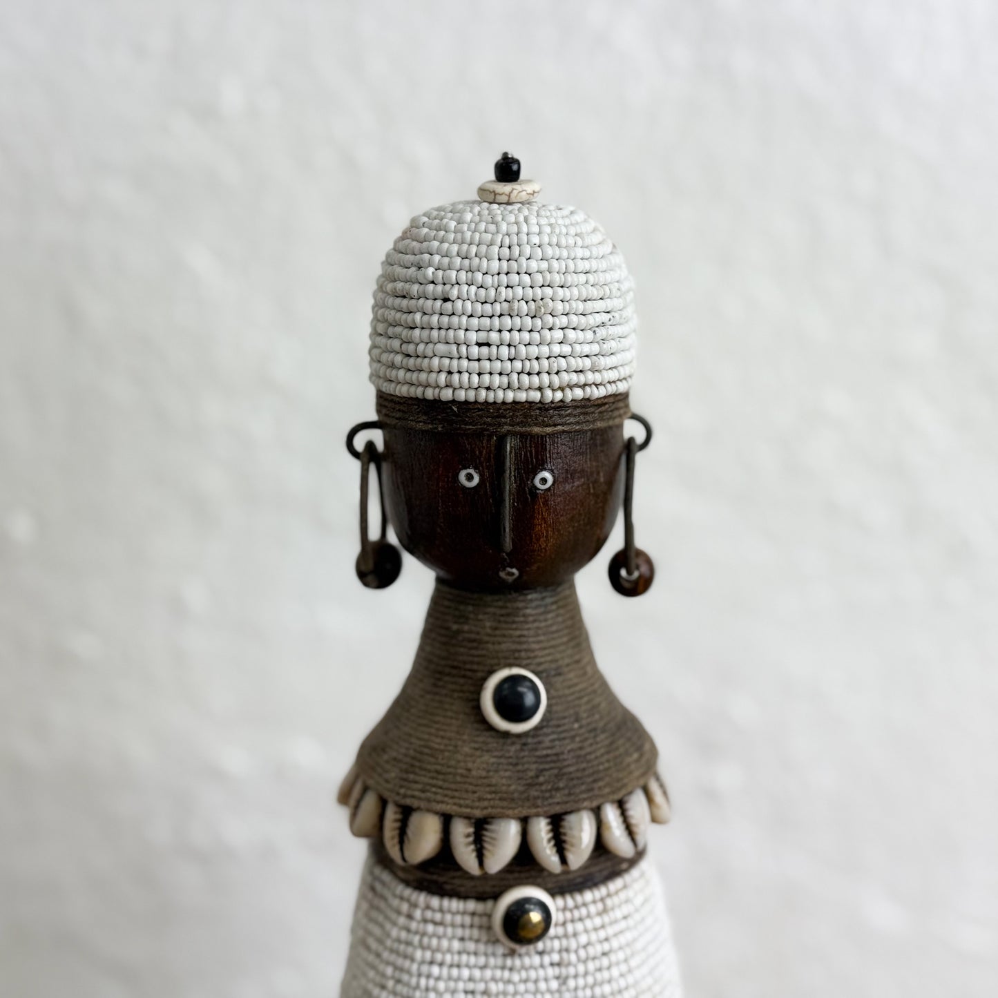 Decorative figure with bead and shell details on a plain background