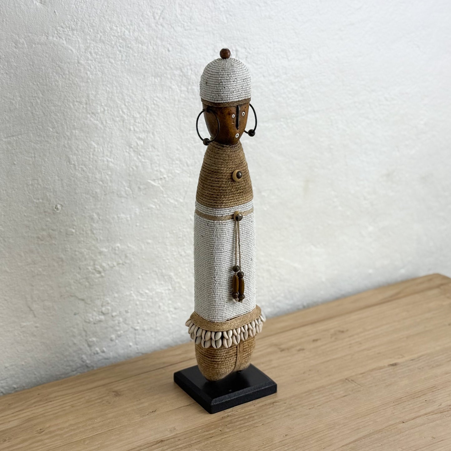 Decorative figure on a stand against a textured white wall