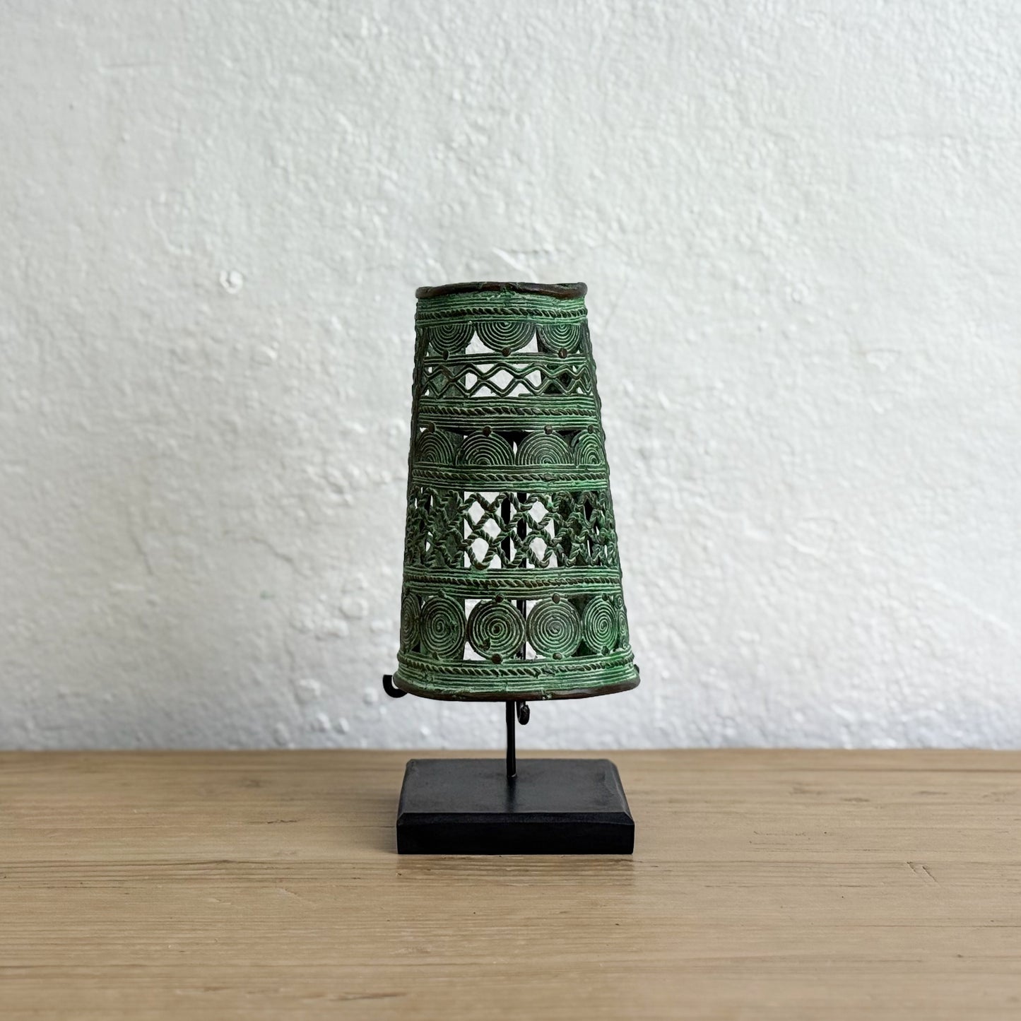 Decorative green metal lantern on a stand against a white wall.