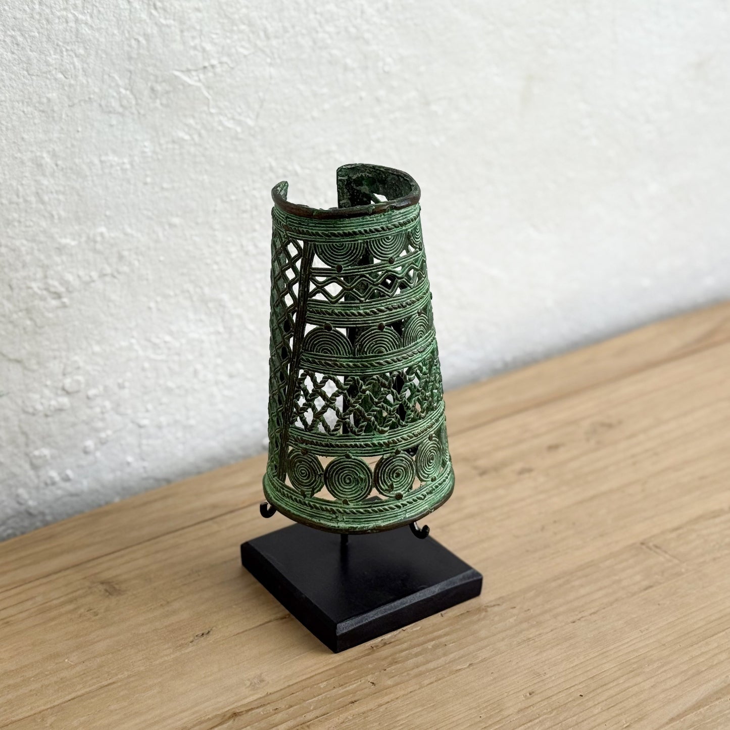 Decorative green metal bell on a black stand against a white wall.