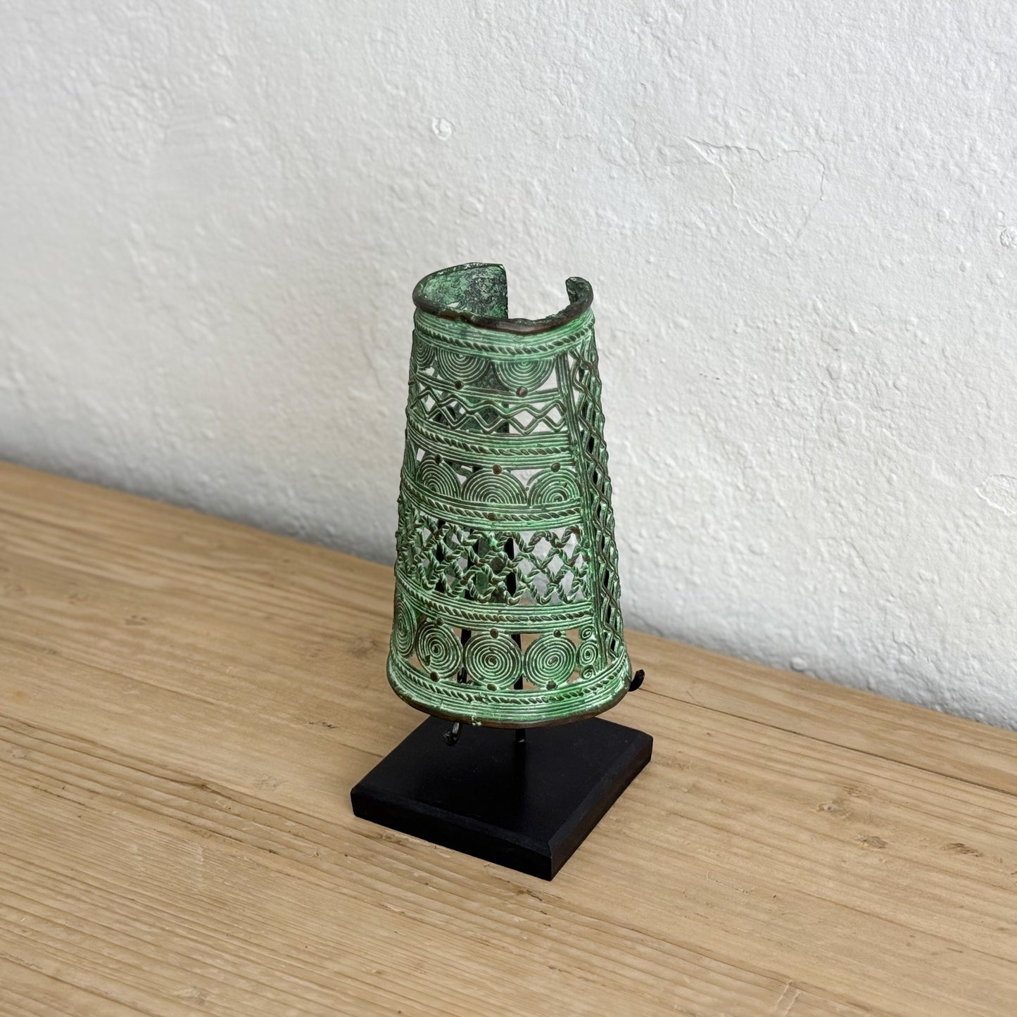 Decorative green metal object on a black stand against a white wall.