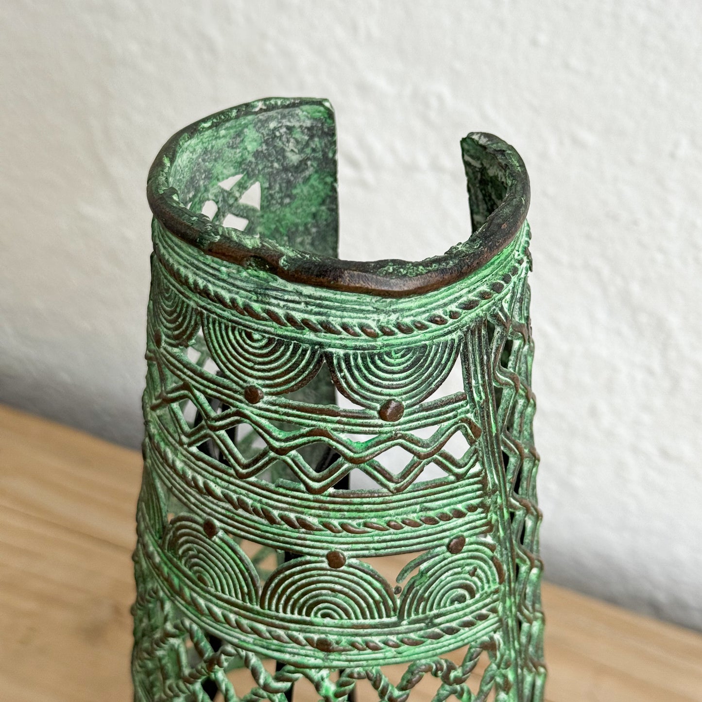 Decorative green metal vase with intricate patterns on a light background