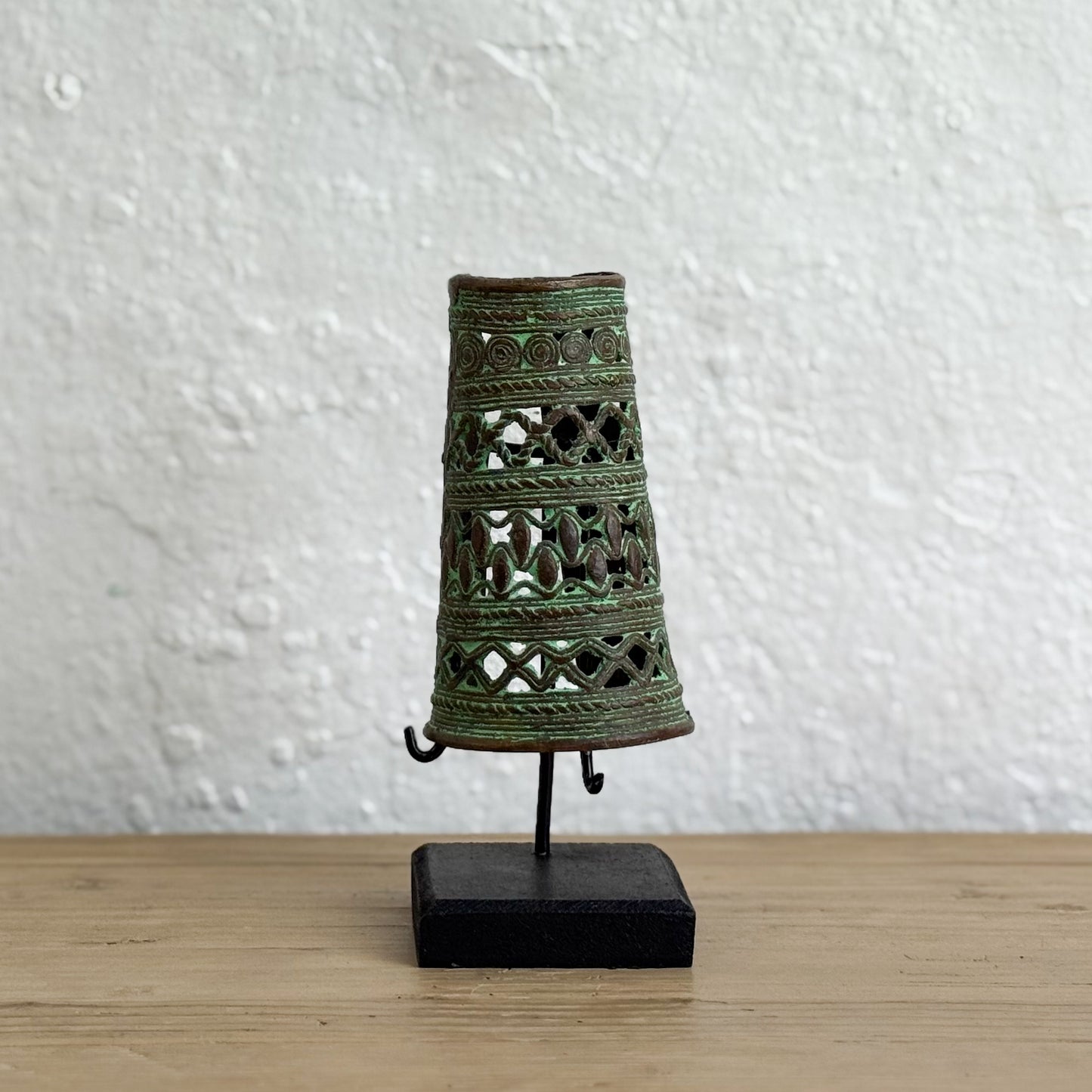 Decorative metal bell with intricate designs on a stand against a white wall.