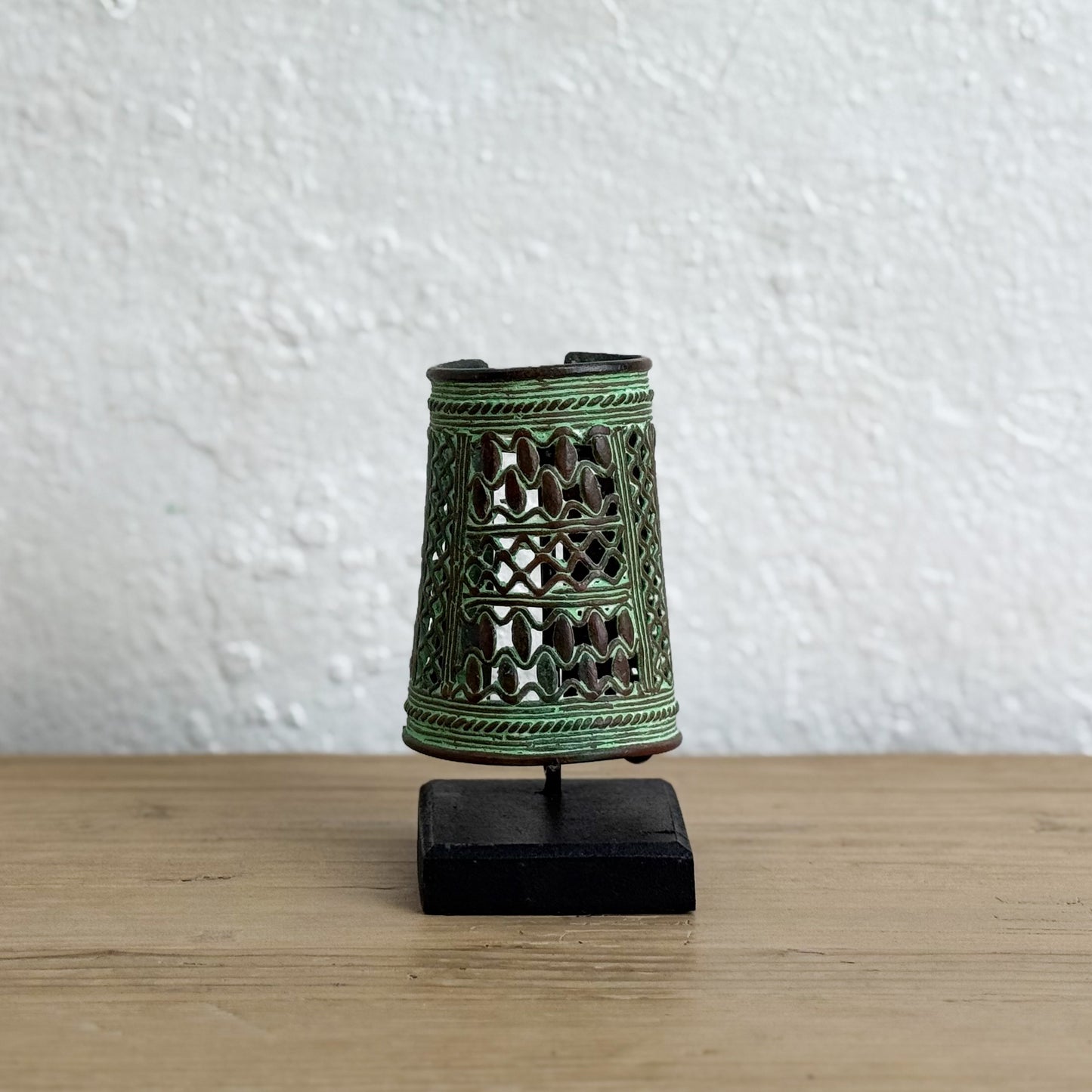 Decorative green metal thimble on a stand against a white wall.