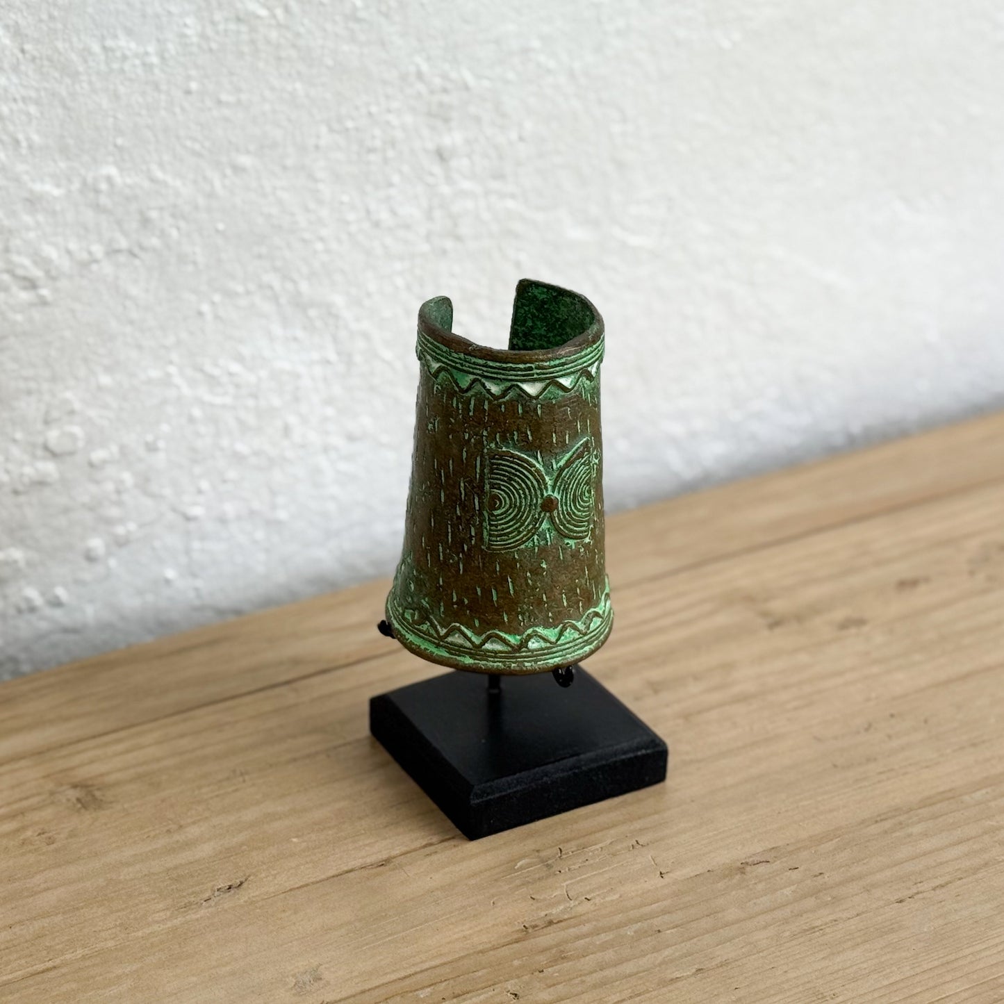 Decorative green vase on a black stand against a white wall.
