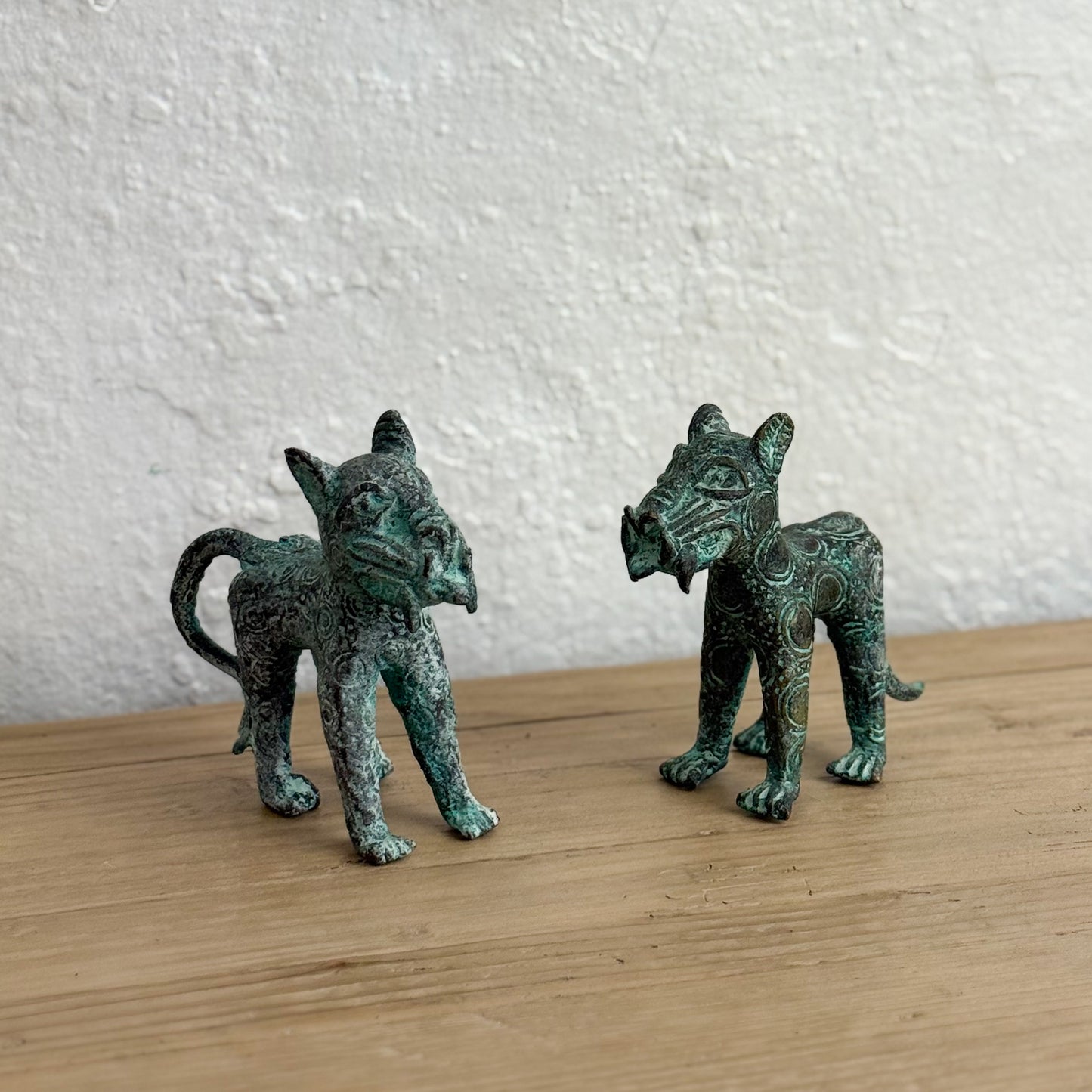 Two green metallic cat figurines on a wooden surface with a textured white wall background.