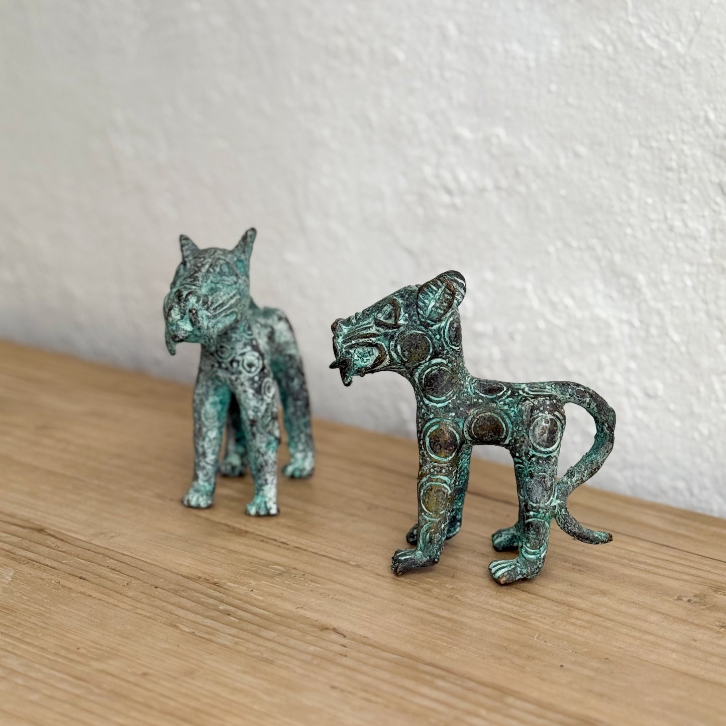 Two metallic cat figurines on a wooden surface with a white wall background