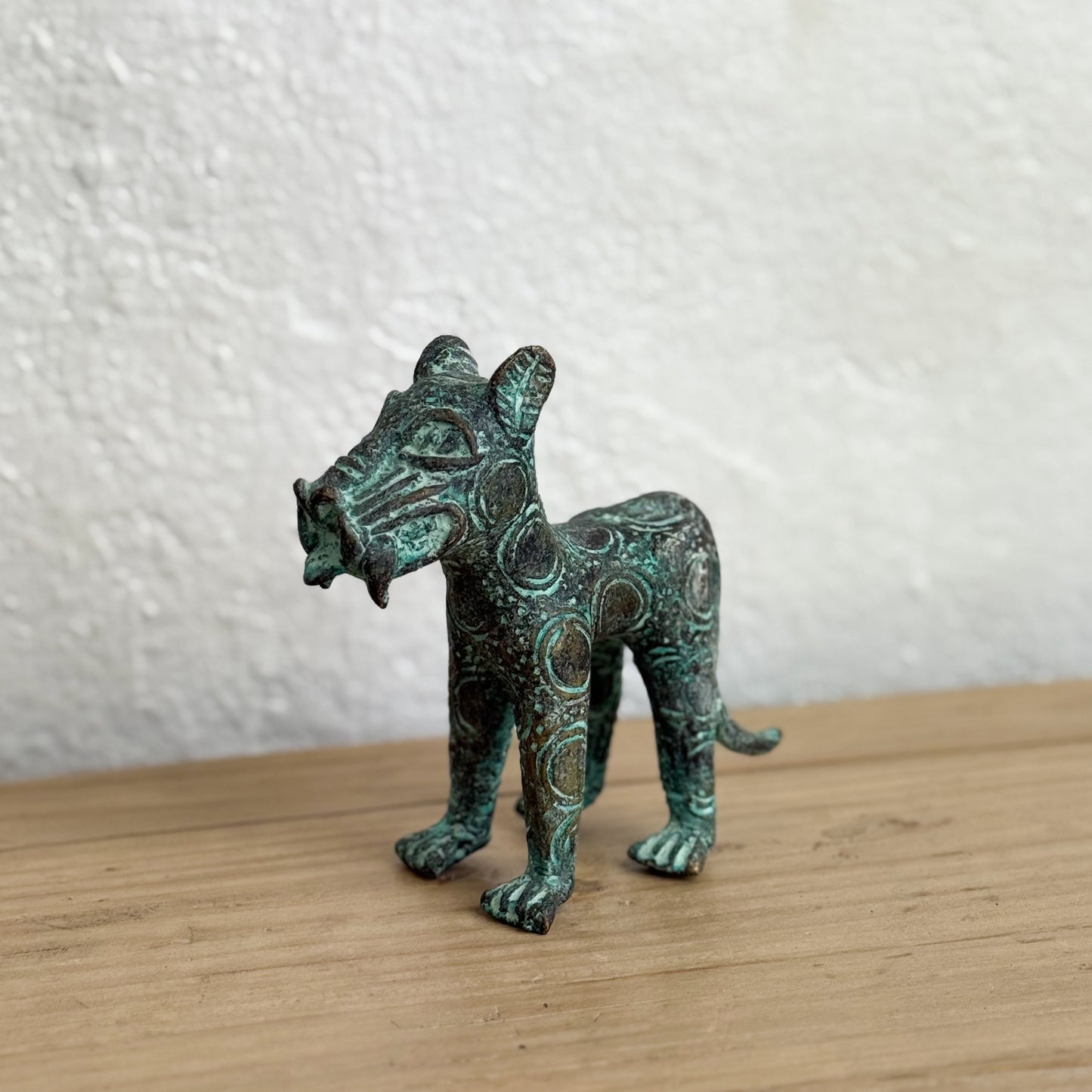 Bronze cat figurine with green patina on a wooden surface