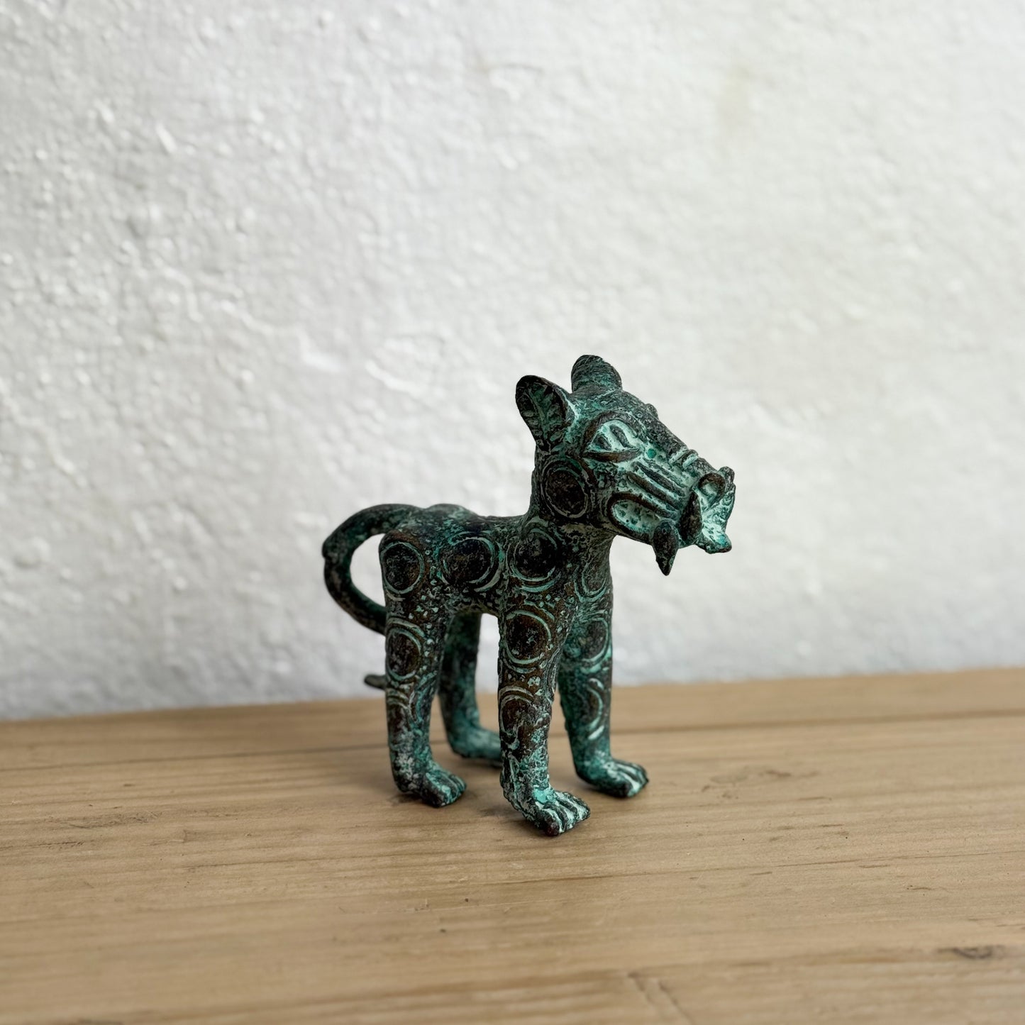 Bronze figurine of a cat on a wooden surface with a textured white wall background