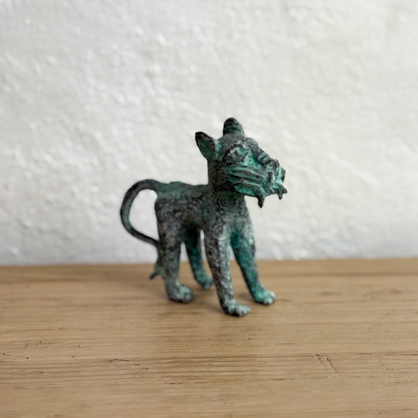 Small bronze figurine of a cat on a wooden surface with a white textured wall background