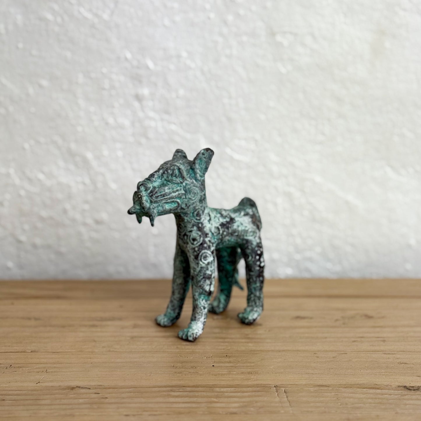 Small bronze figurine of a dog on a wooden surface with a white textured wall background