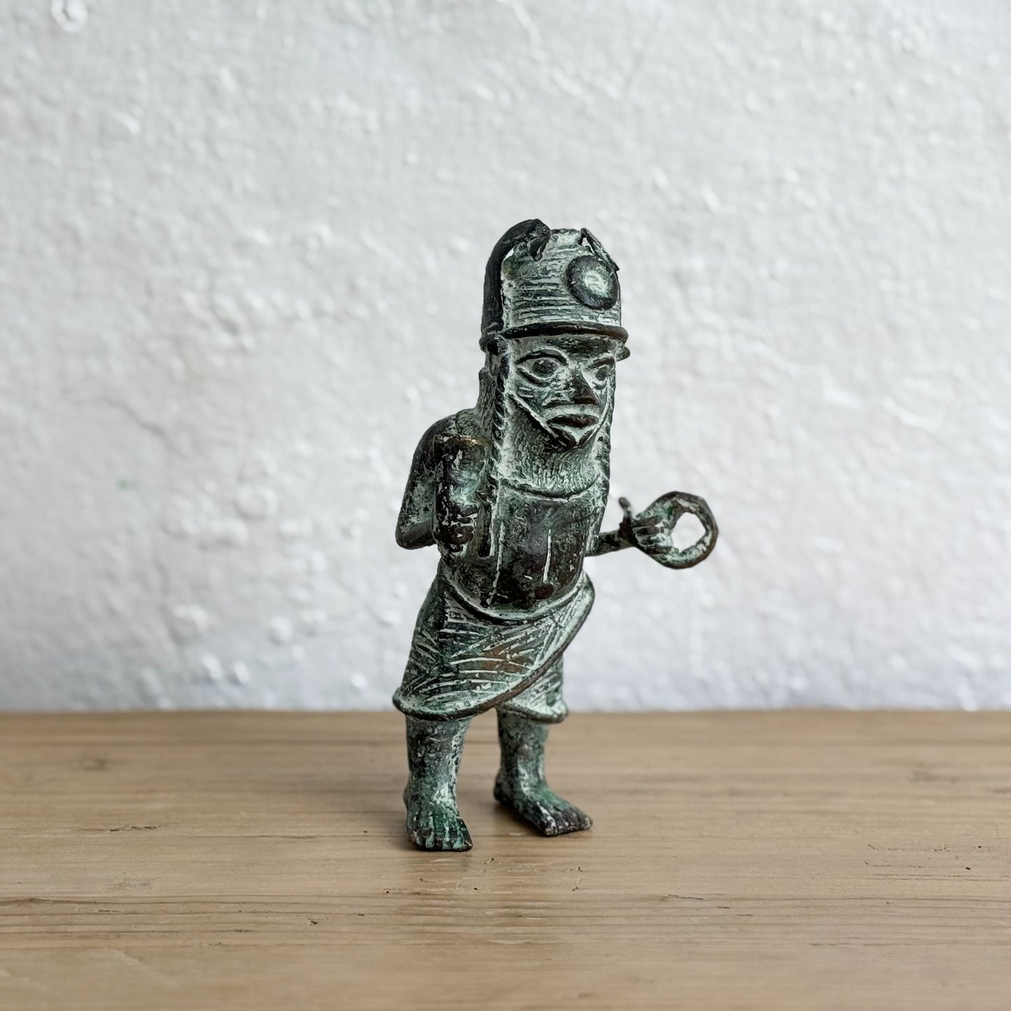 Bronze figurine of a warrior on a wooden surface with a white wall background